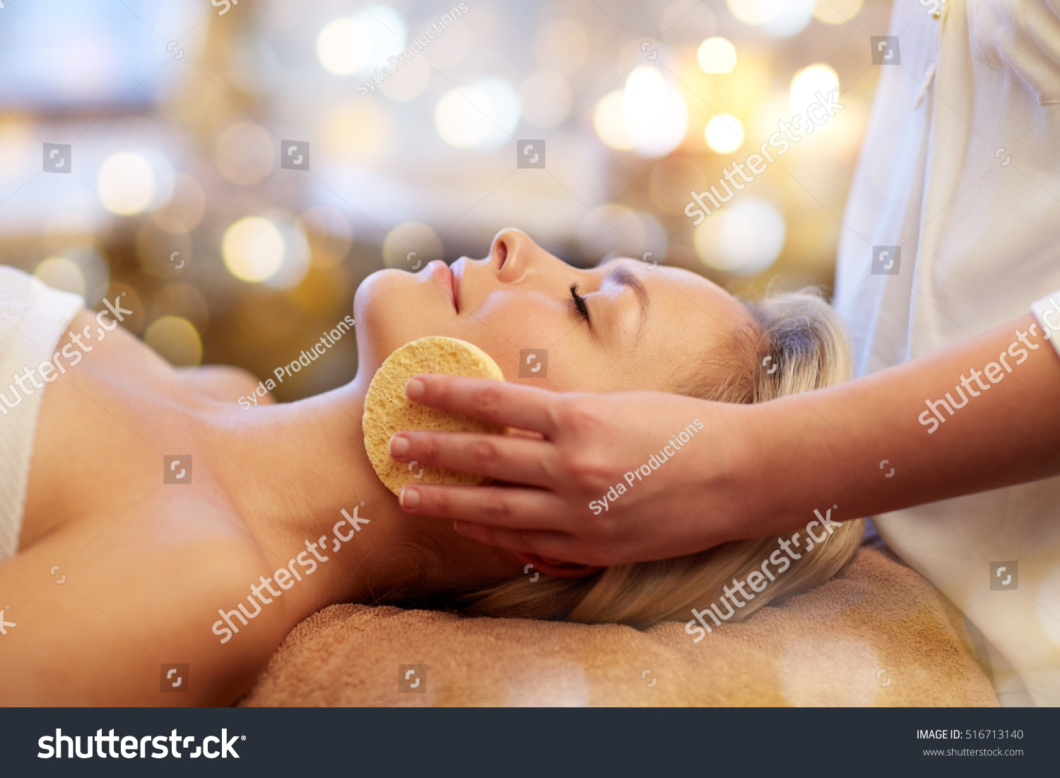 people, beauty, spa, healthy lifestyle and relaxation concept - close up of beautiful young woman lying with closed eyes and having face massage with sponge in spa #516713140