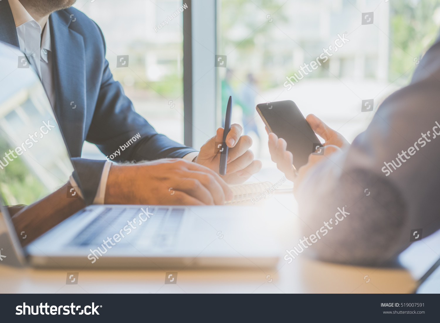 Business meeting, interview. Side view,closeup of man's hands, in hands of one of businessman smartphone, in hands of other businessman pen and notebook, on table is a laptop,film effect #519007591