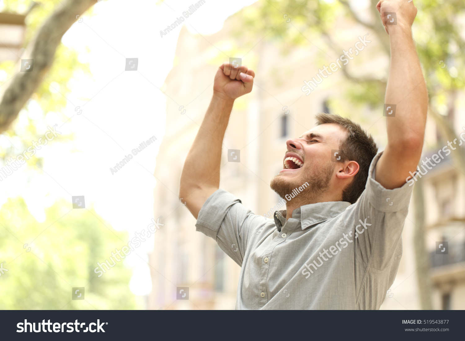 Portrait of an excited man raising arms in the street with buildings in the background #519543877