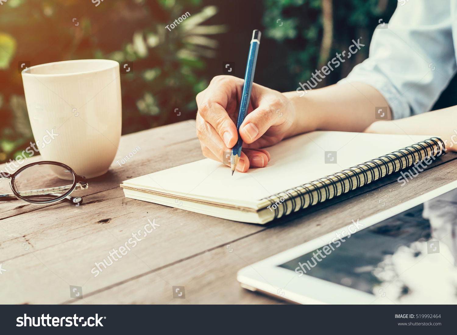 Woman hand with pencil writing on notebook at coffee shop. Woman working in outdoor at coffee shop. #519992464