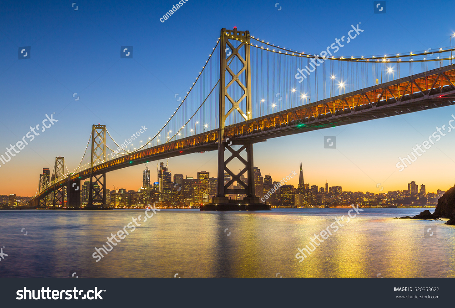 Classic panoramic view of famous Oakland Bay Bridge with the skyline of San Francisco in the background illuminated in beautiful twilight after sunset in summer, California, USA #520353622
