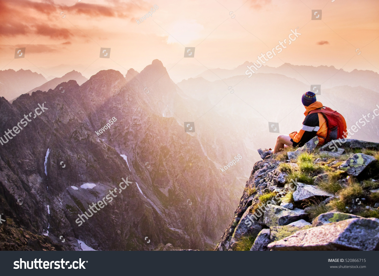 Young male hiker with backpack relaxing on top of a mountain during calm summer sunset - scenery from vacation - photo with space for your montage. #520866715