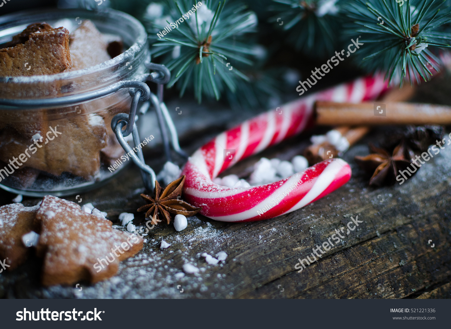 Christmas homemade gingerbread cookies and red candy cane on old wooden table with fir tree. Christmas treats concept. Christmas moody style background. Selective focus. Copy space. Toned image. #521221336