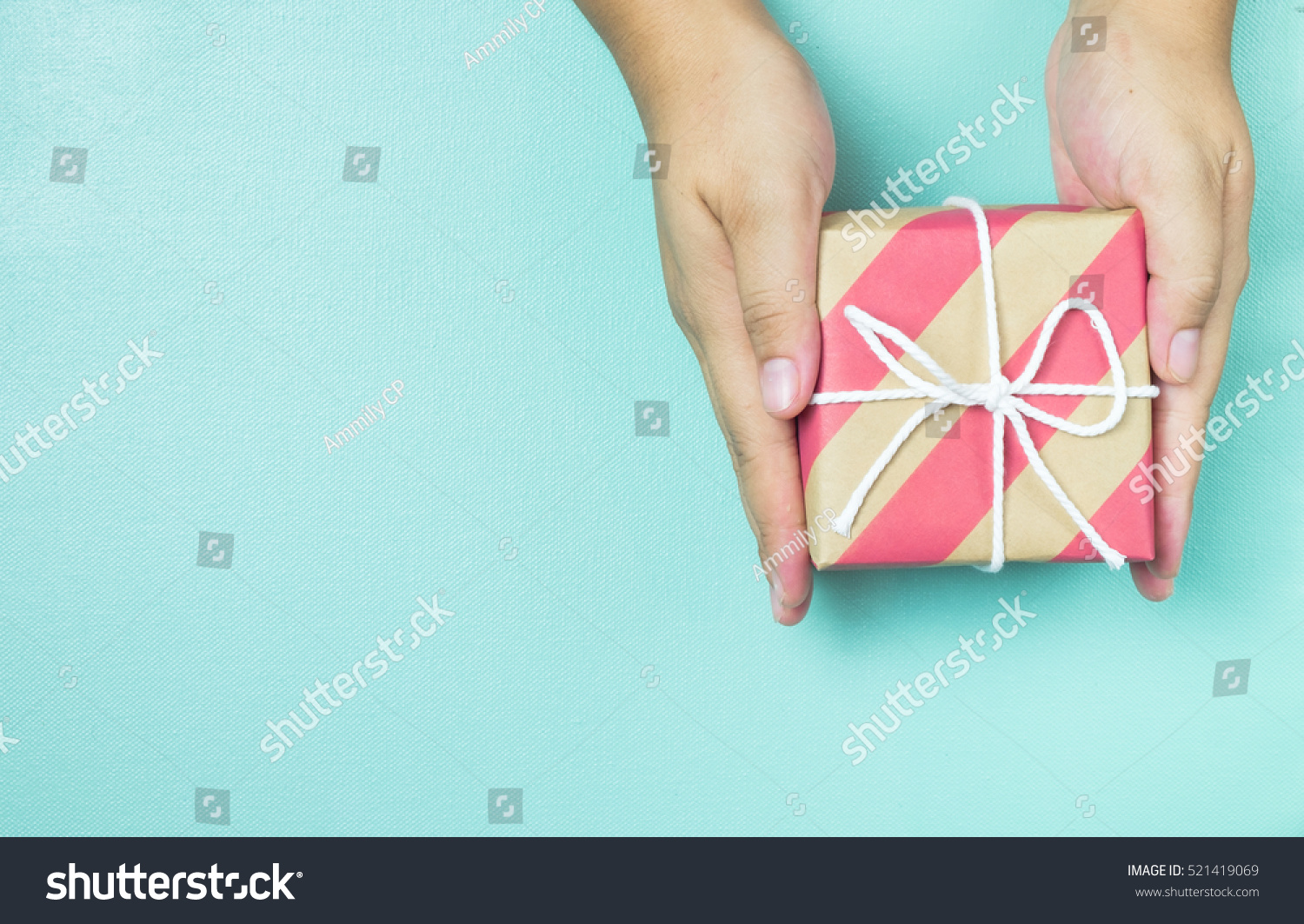 Hands holding craft paper gift box with as a present for Christmas, new year, valentine day or anniversary on blue background, top view #521419069