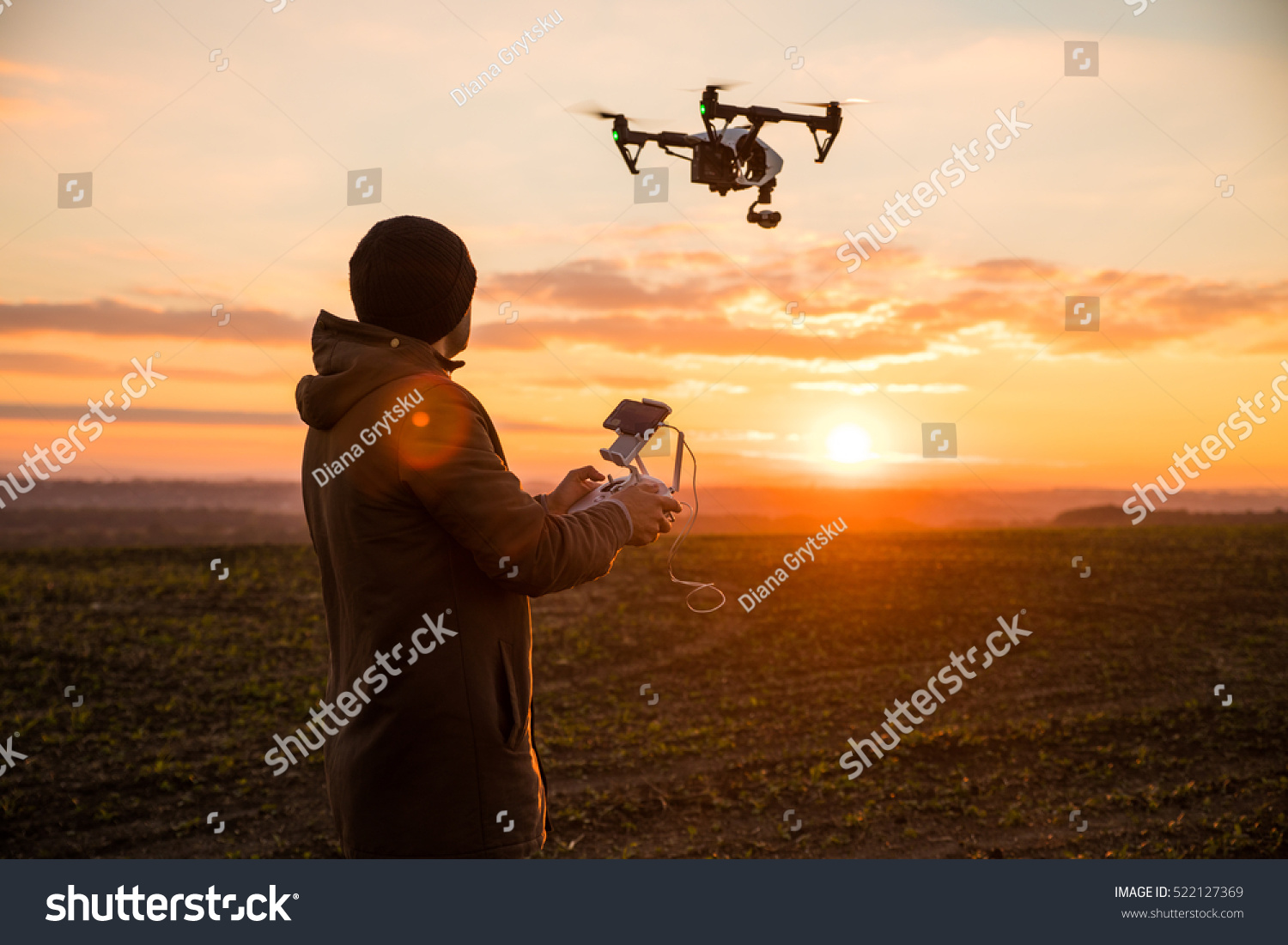 Man operating a drone with remote control. Dark silhouette against colorful sunset. Soft focus. #522127369