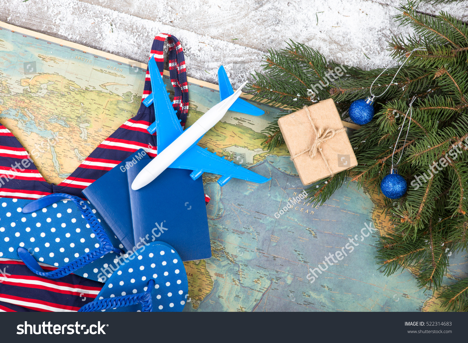 Christmas concept - travel. Fir branches with snow, maps, swimsuit, passports, gift box, flops and toy airplane #522314683