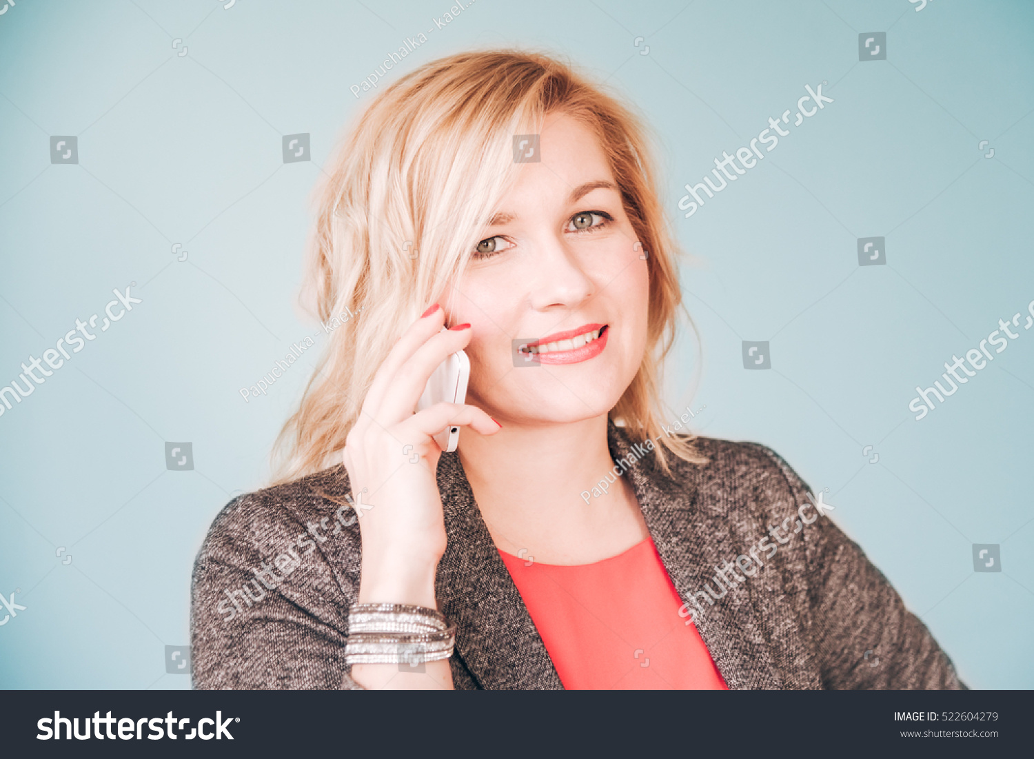 Pretty happy smiling woman in red blouse and business costume jacket communicating over white smartphone against pale teal blue background #522604279