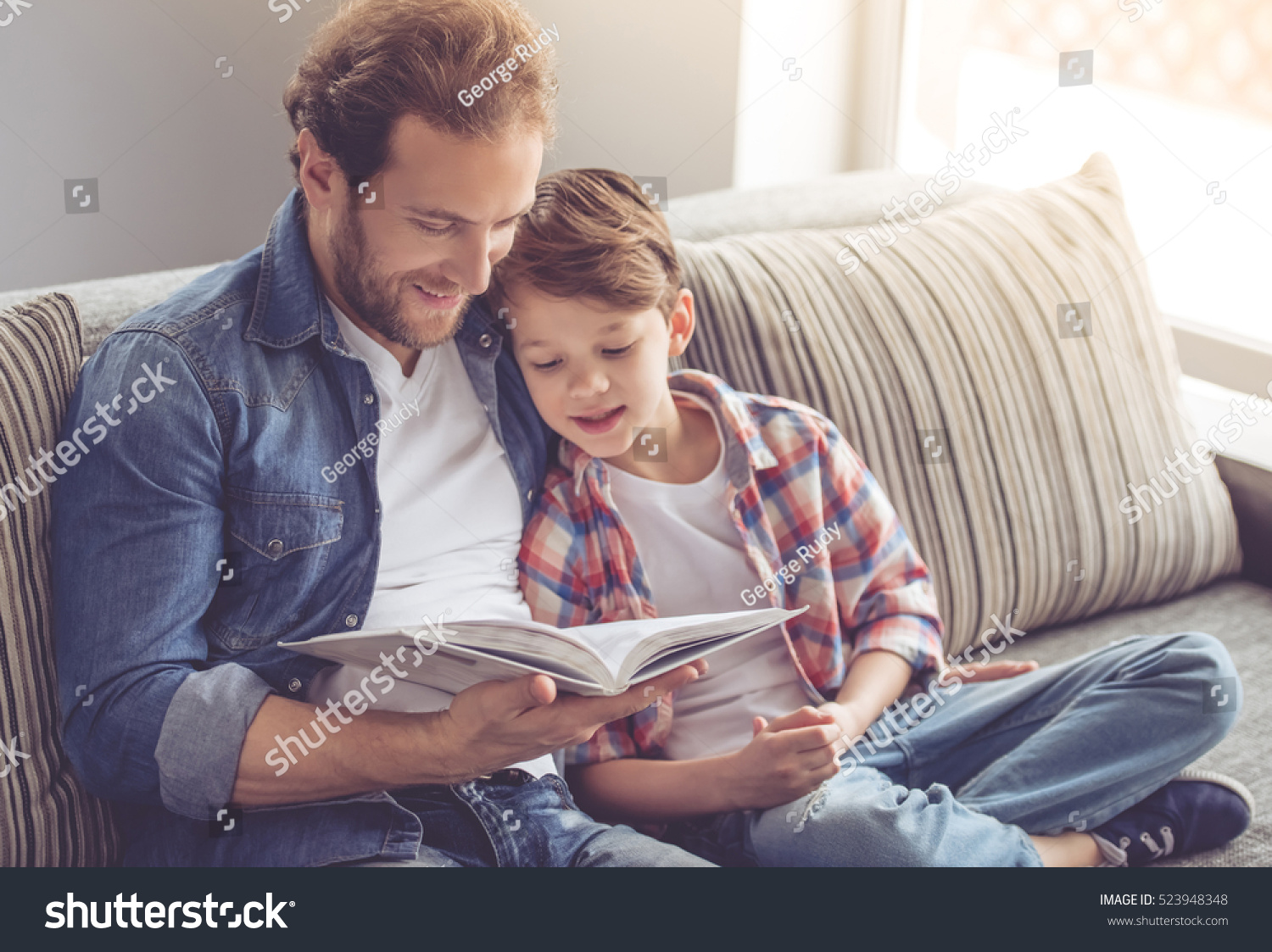 Father and son are reading a book and smiling while spending time together at home #523948348