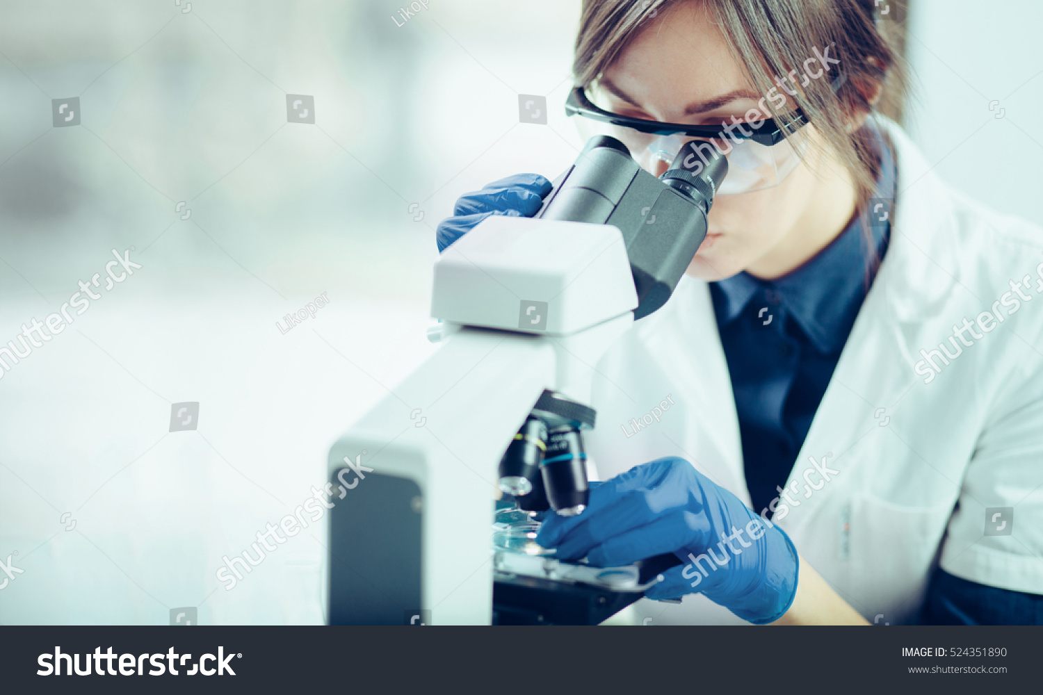 Young scientist looking through a microscope in a laboratory. Young scientist doing some research. #524351890