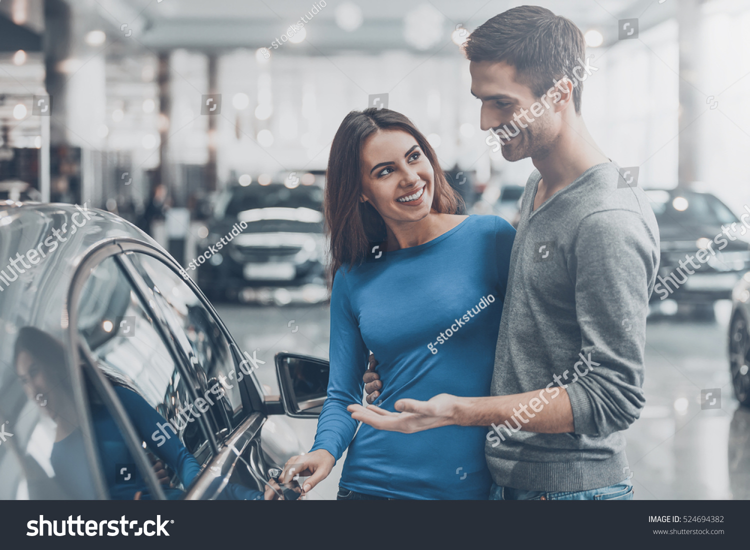 It is the one car I want! Beautiful young couple standing at the dealership choosing the car to buy #524694382