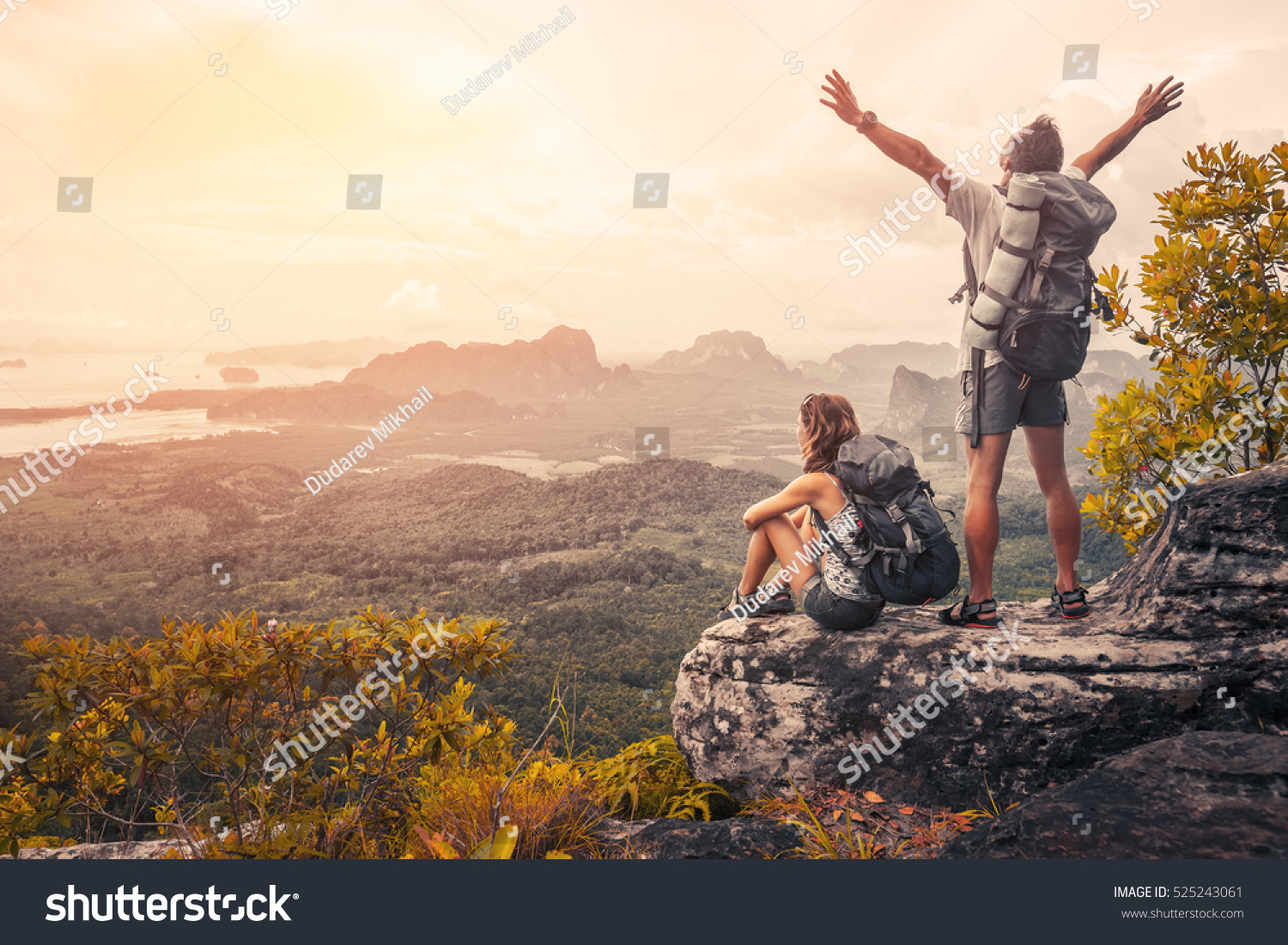 Hikers with backpacks relaxing on top of a mountain and enjoying the view of valley at sunset #525243061