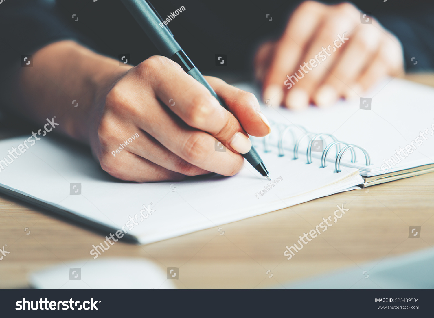 Close up of woman's hands writing in spiral notepad placed on wooden desktop with various items #525439534