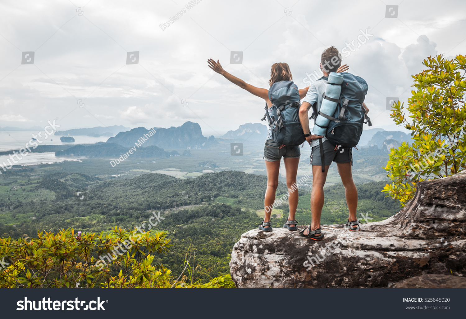 Hikers with backpacks relaxing on top of a mountain and enjoying the view of valley #525845020