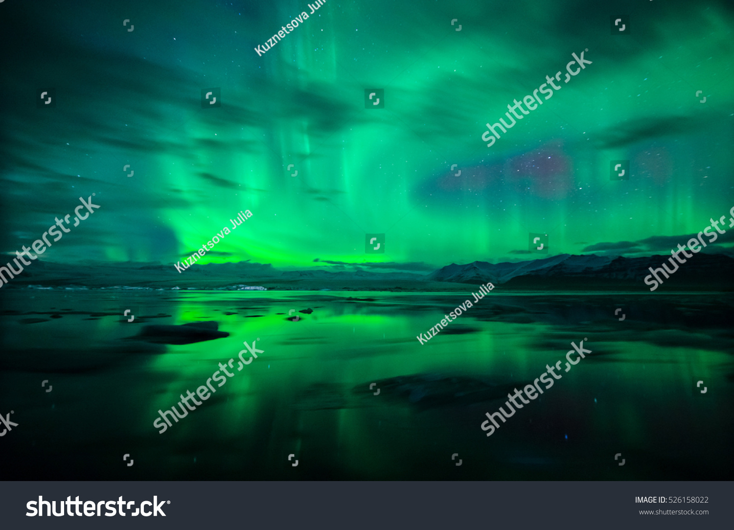 Northern lights (Aurora Borealis) and fast moving clouds reflected over water and icebergs  of glacial lagoon Jokulsarlon in Iceland. #526158022