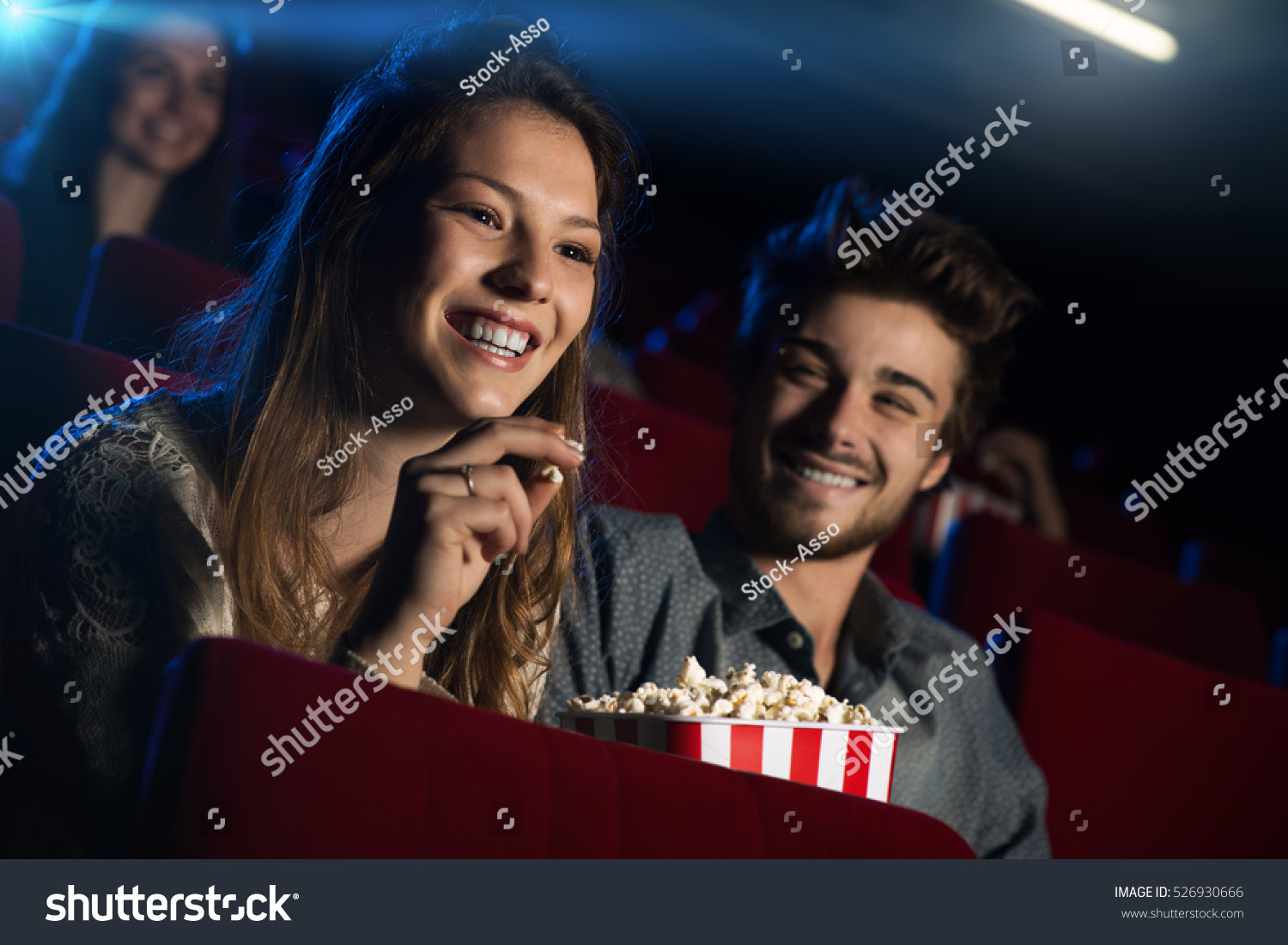 Young loving couple at the cinema watching a movie and smiling, people sitting on background #526930666