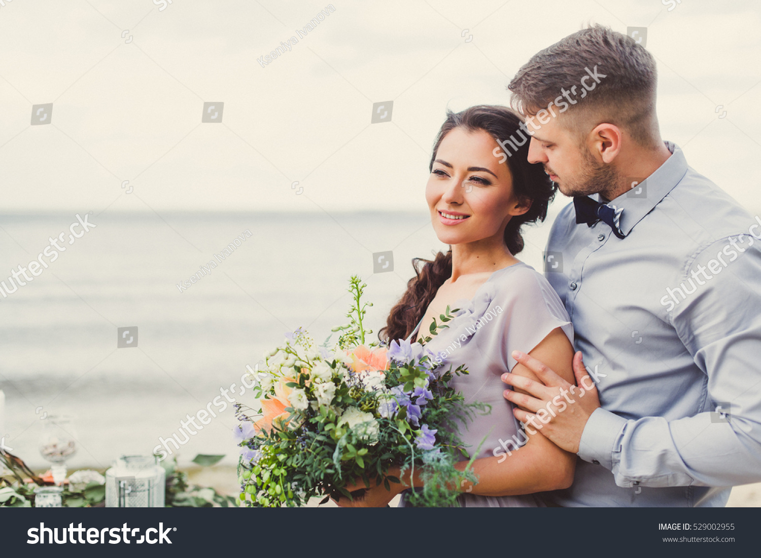 Bride and groom on the beach near the table decorations. Bride holding a beautiful bouquet. #529002955