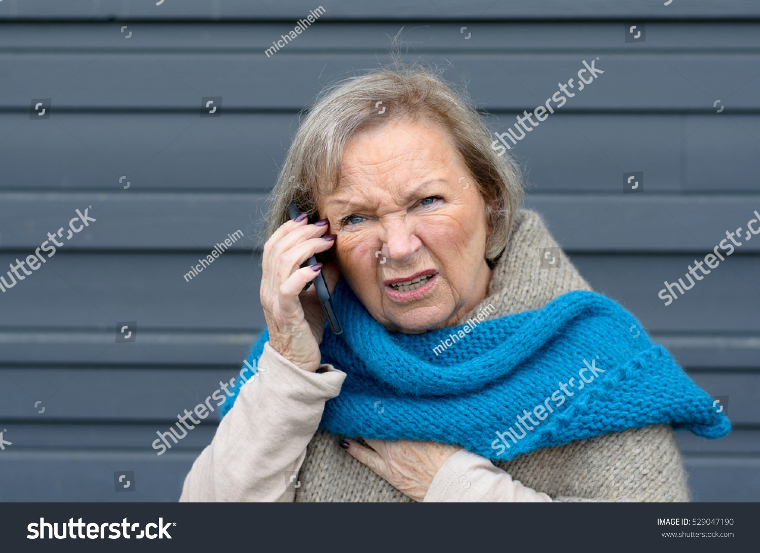 Confused elderly woman chatting on her mobile phone frowning in puzzlement as she listens to the conversation #529047190