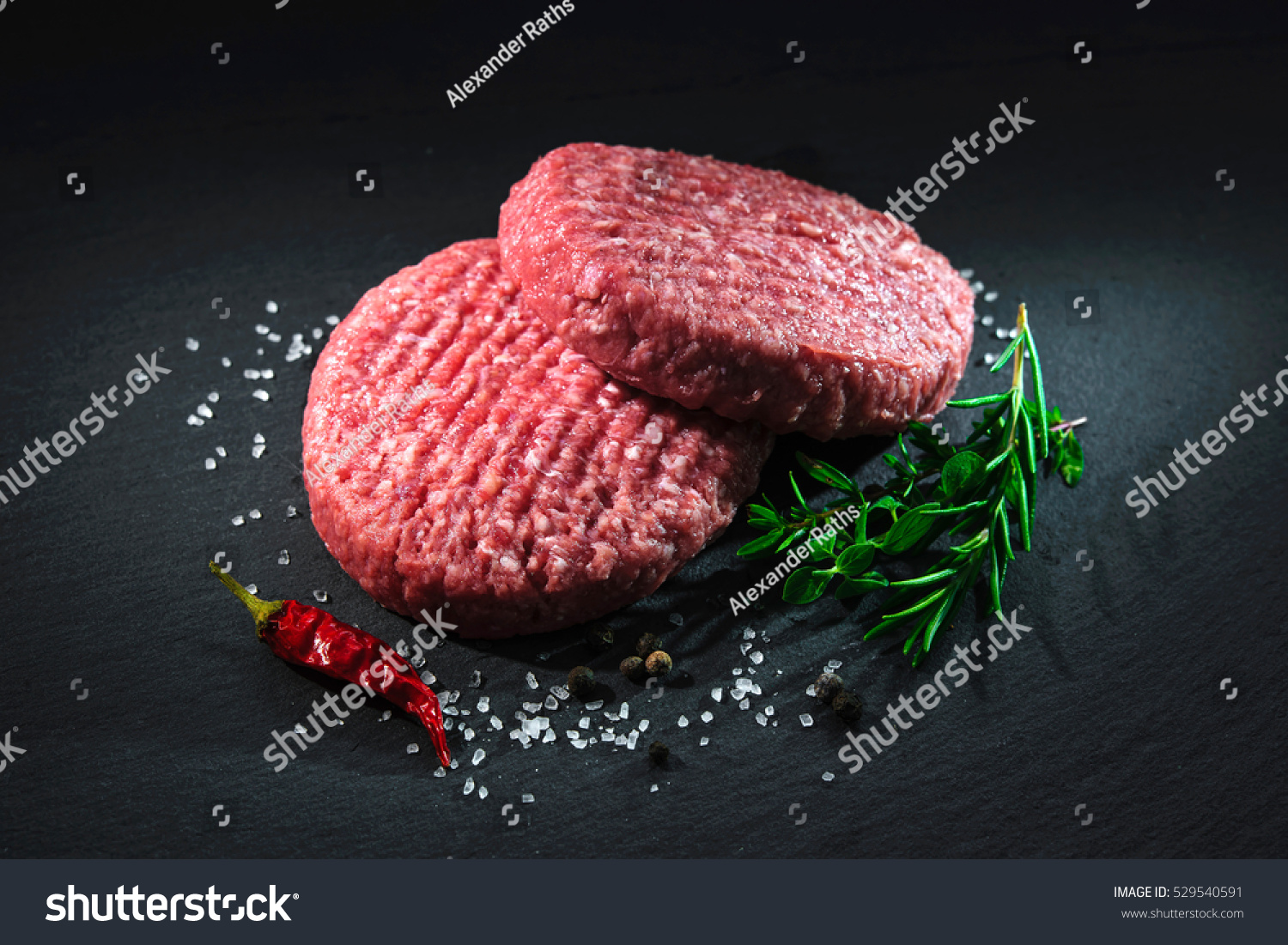 Raw beef hamburger patties with herbs and spices on dark slate plate #529540591