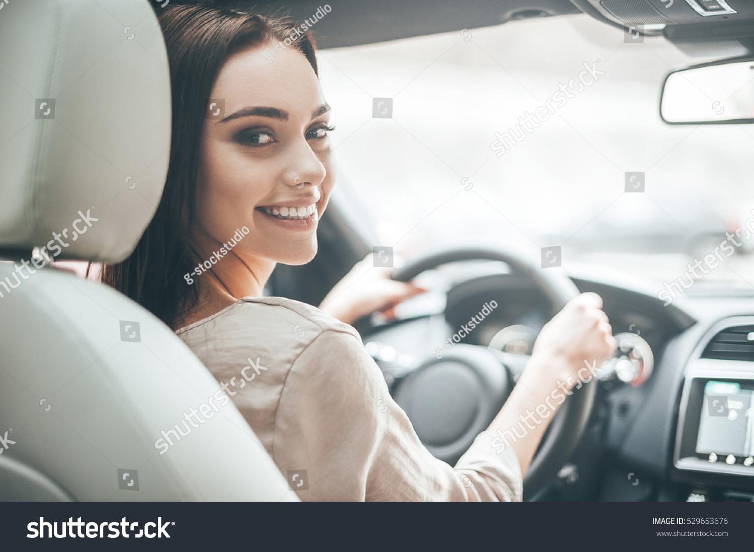 Confident and beautiful. Rear view of attractive young woman in casual wear looking over her shoulder while driving a car  #529653676