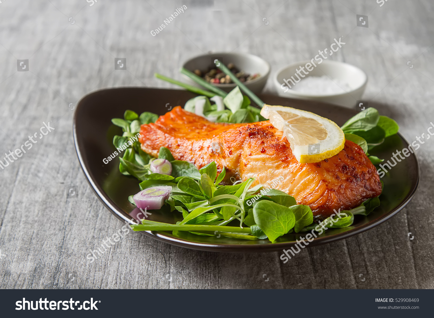 One piece of baked salmon grilled pepper lemon and salt on a brown plate with lettuce leaves. wood background #529908469