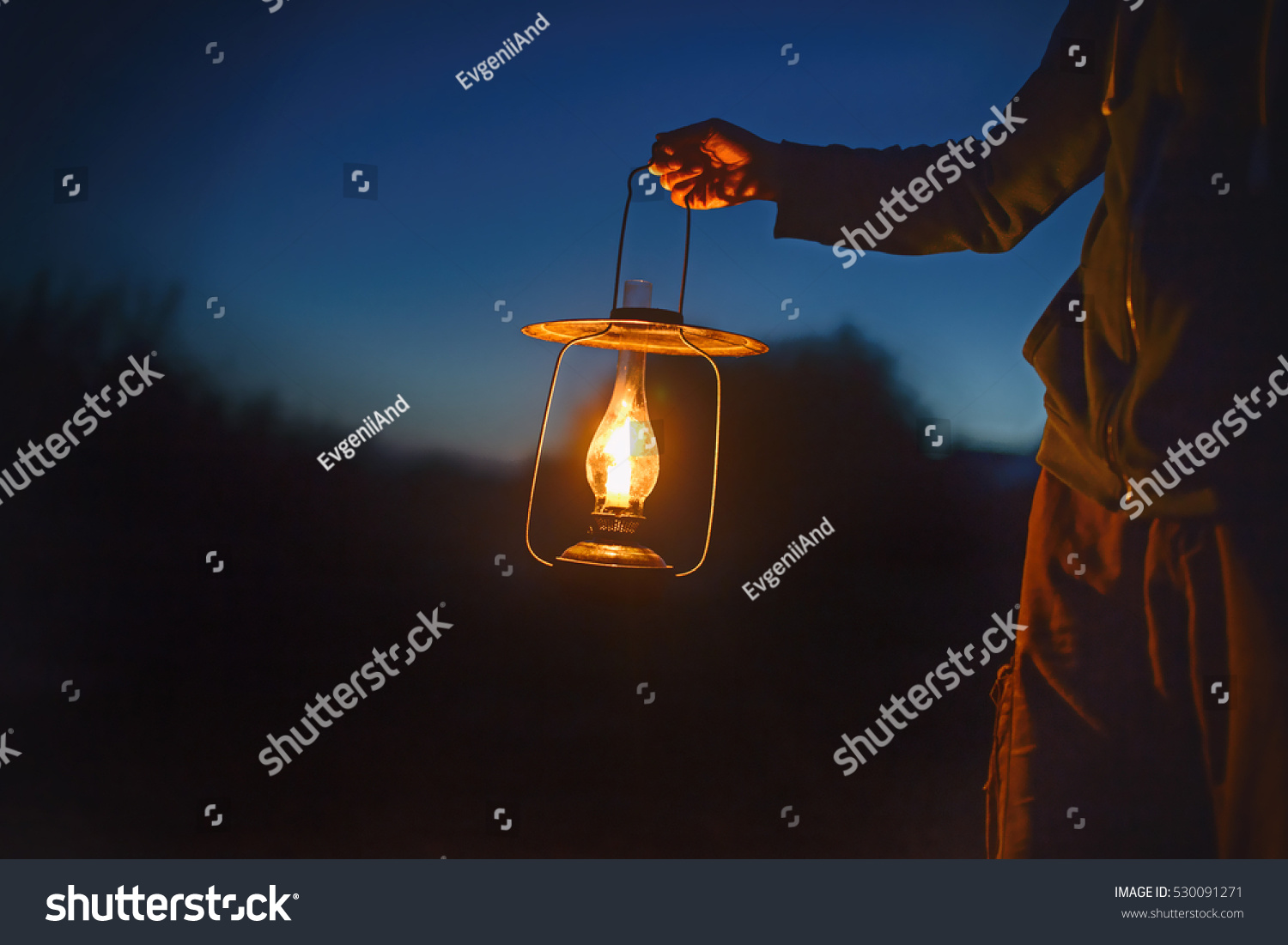 man holding the old lamp with a candle outdoors. hand holds a large lamp in the dark. ancient lantern with a candle illuminates the way on a night #530091271