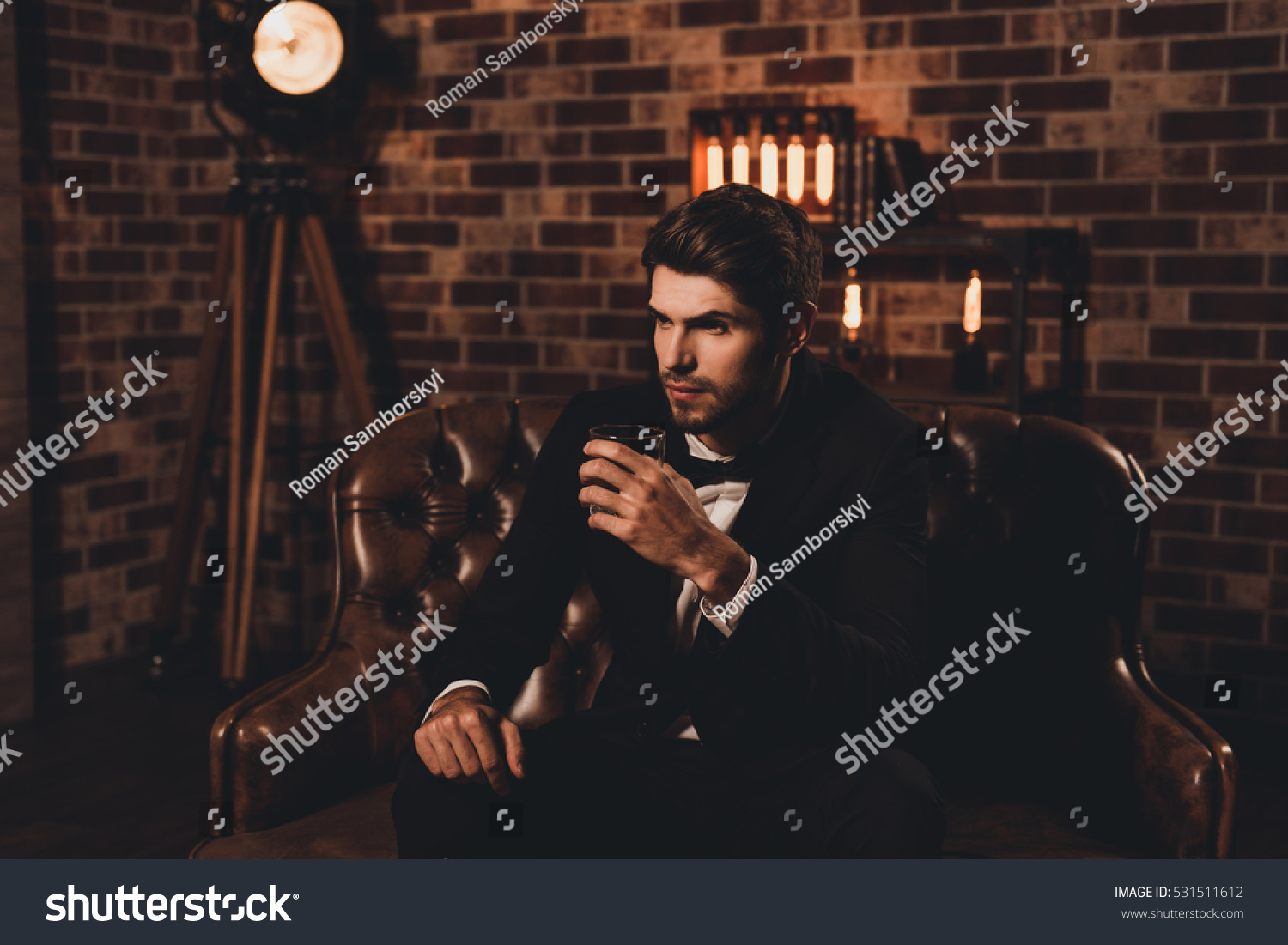 Handsome young man in elegant suit with glass of whiskey relaxing on sofa #531511612