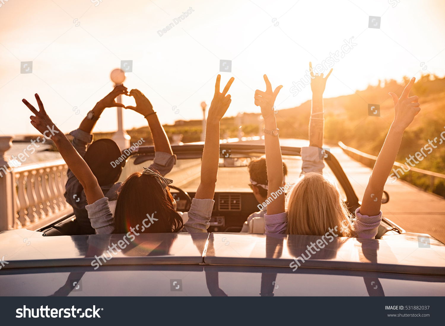 Group of happy young friends in cabriolet with raised hands driving on sunset #531882037