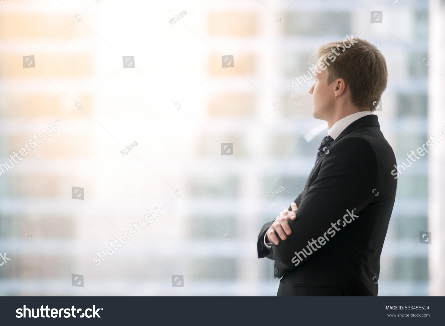 Successful businessman in suit standing in office with hands crossed on chest, looking through window at big city buildings, planning new projects, waiting for meeting to start. Copy space for text #533456524