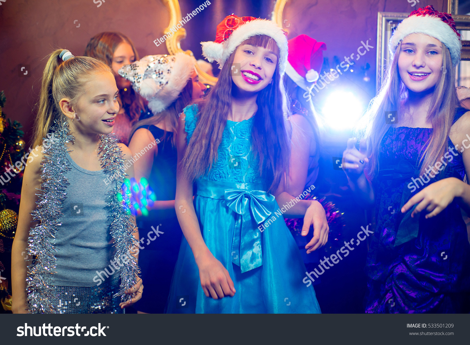 Group of cheerful young girls celebrating Christmas near the Christmas tree with lights #533501209