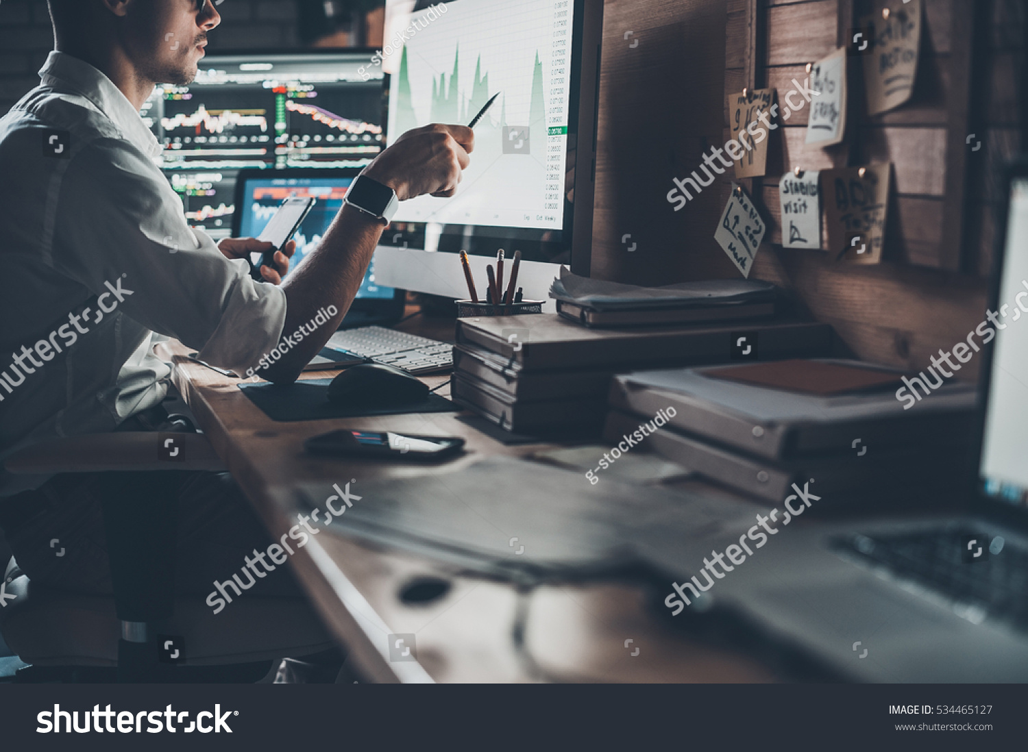 Analyzing data. Close-up of young businessman looking at monitor while sitting at the desk in creative office  #534465127