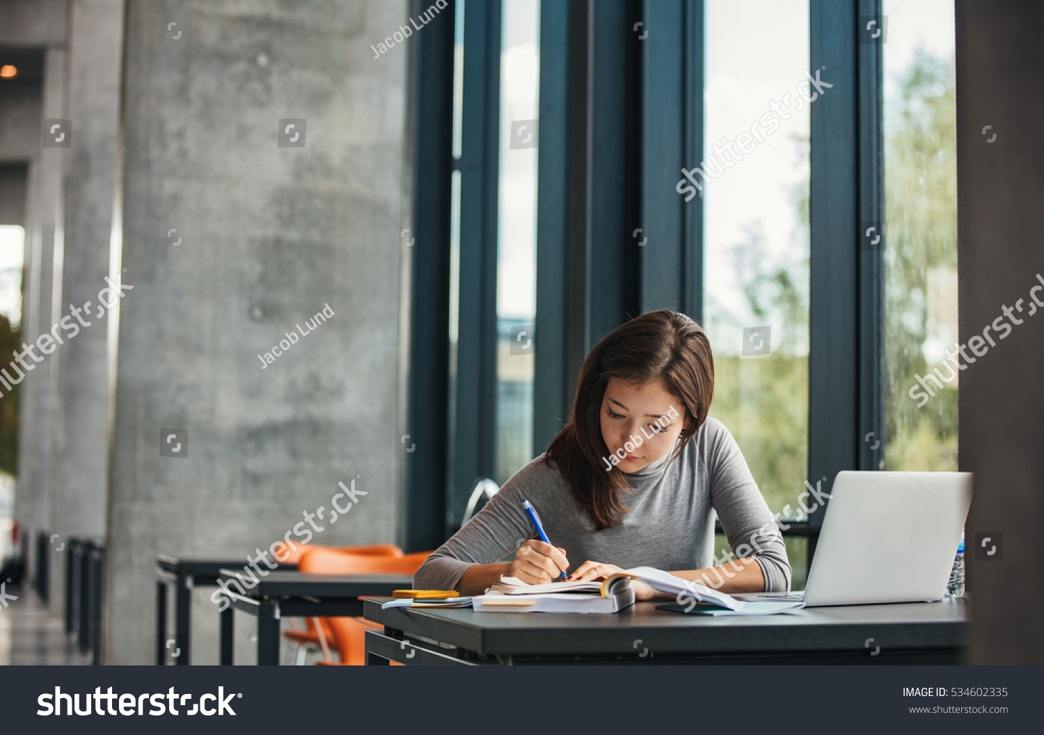 Shot of young asian female student sitting at table and writing on notebook. Young female student studying in library. #534602335