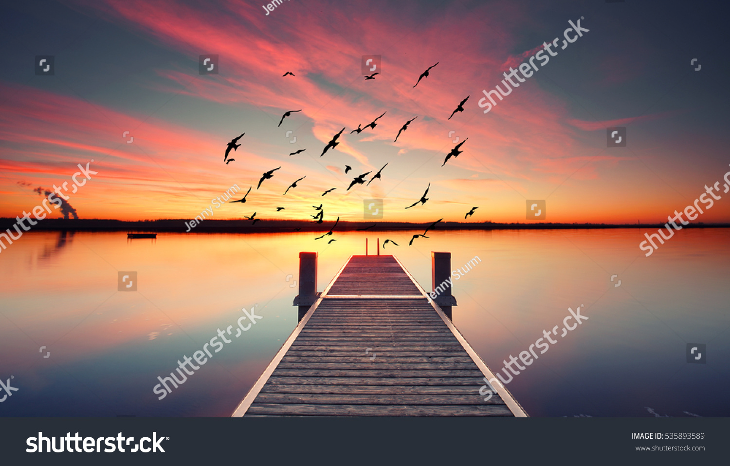 Perspective view of a wooden pier on the pond at sunset with perfectly specular reflection #535893589