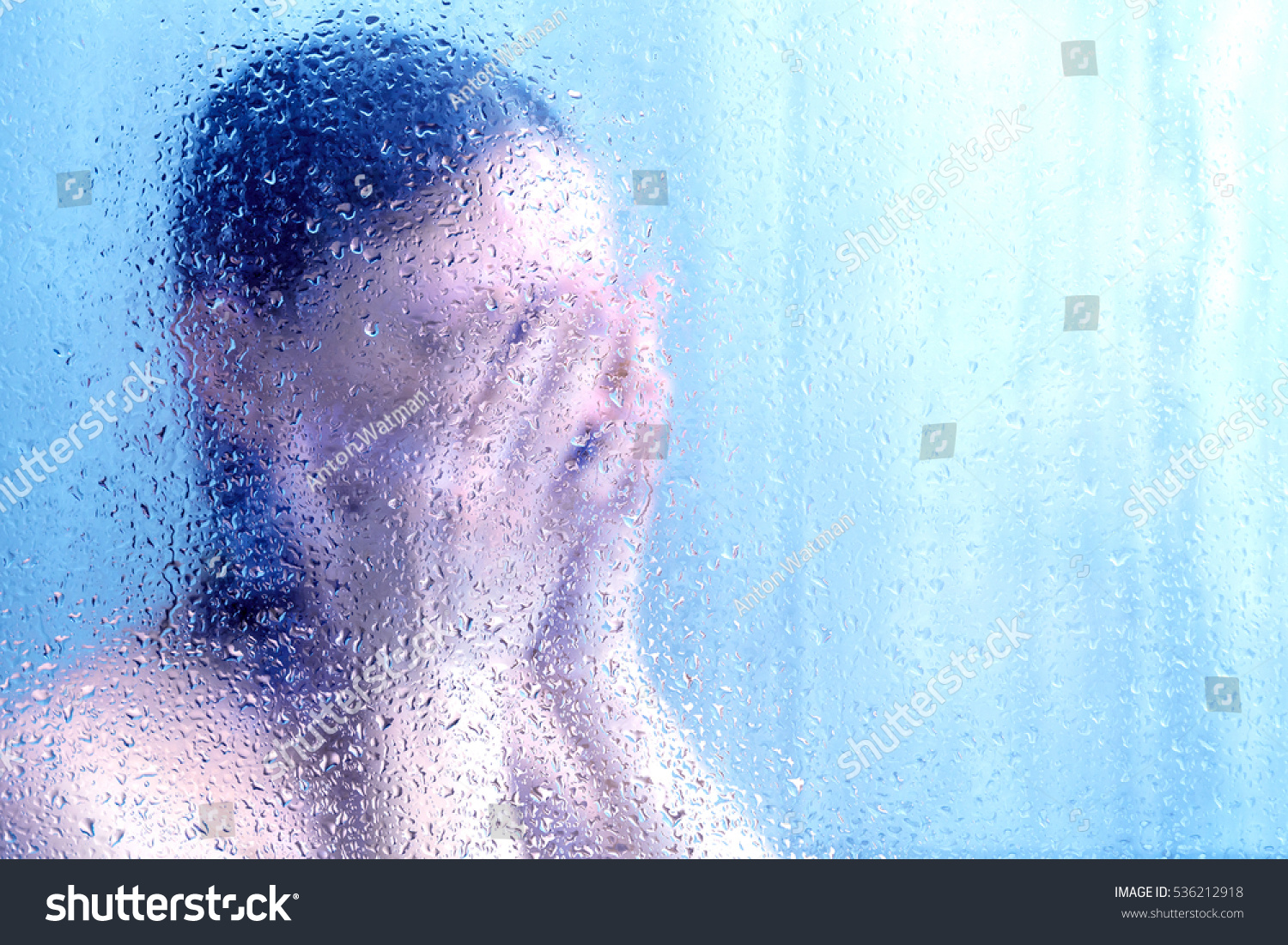 Beautiful woman in the shower behind glass with drops, blue glow #536212918