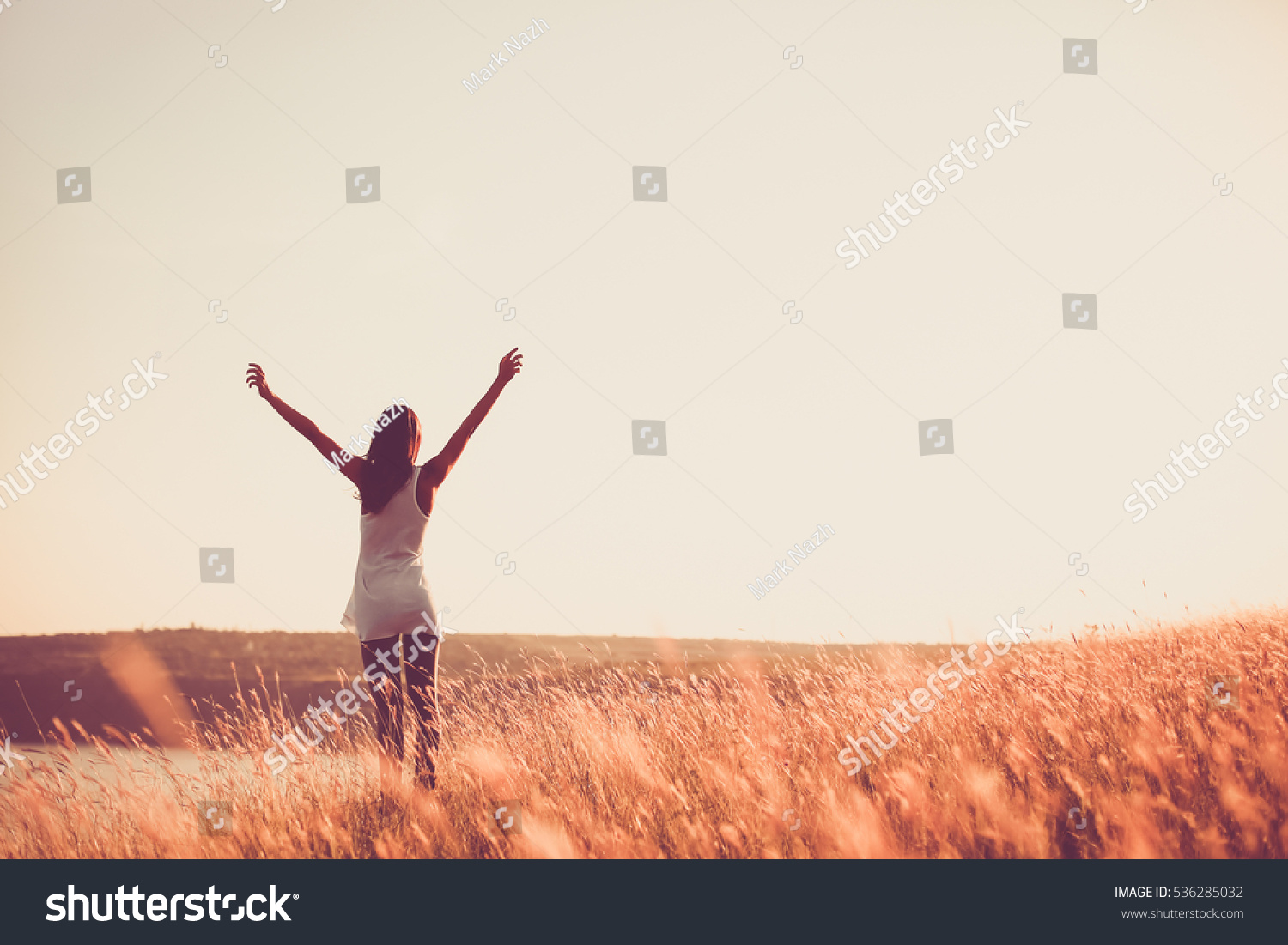 Free woman raising arms to golden sunset. Freedom and success concept. Girl relaxing and enjoying nature with copy space. Toned film effect #536285032