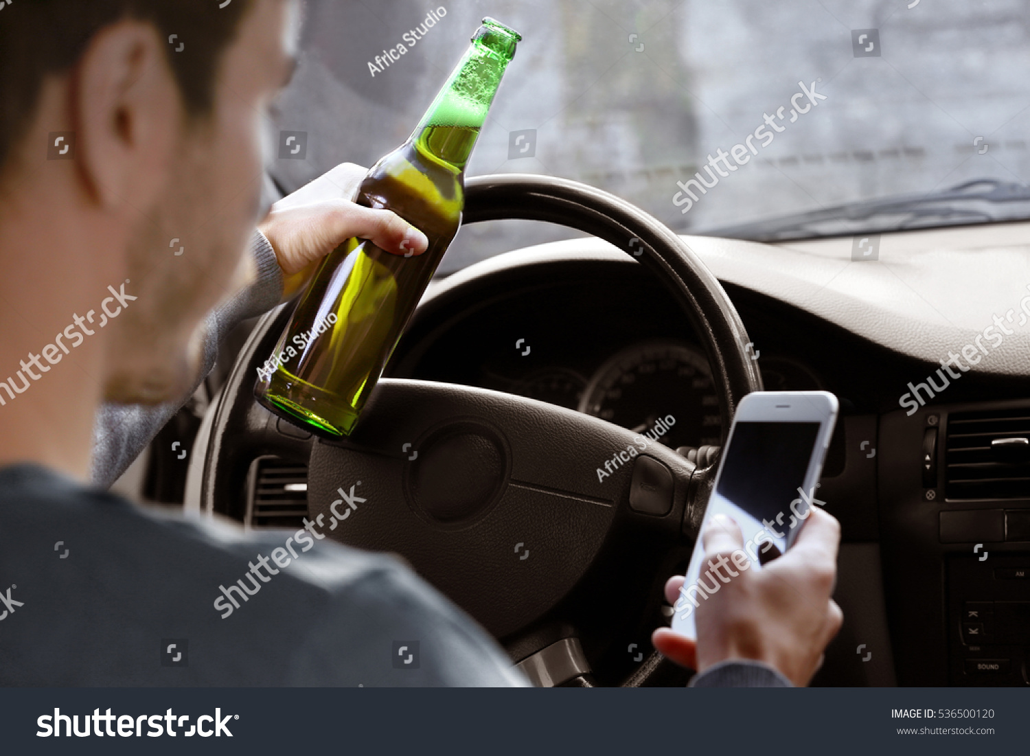 Man holding mobile phone and bottle of beer while driving car, closeup. Don't drink and drive concept #536500120