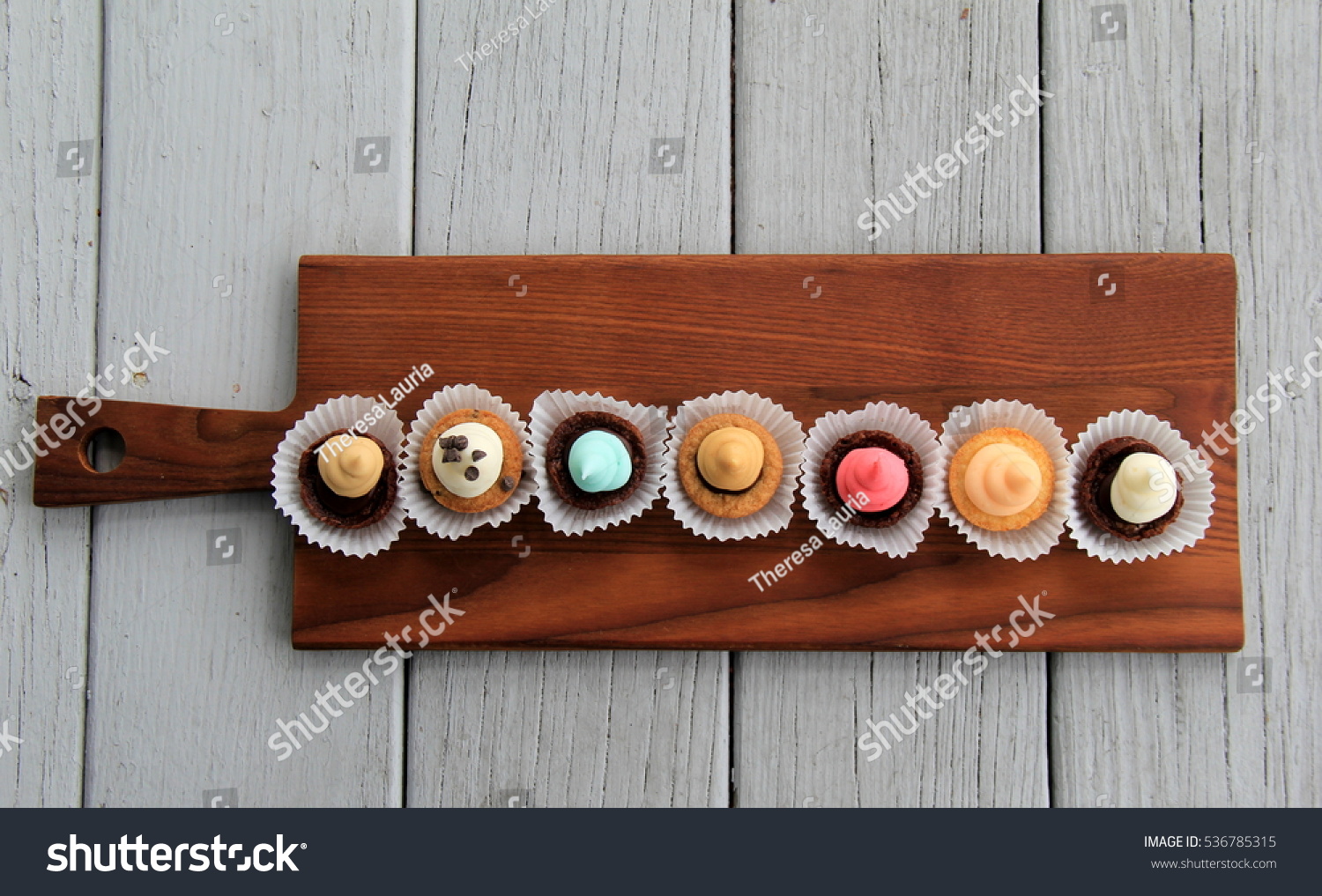Seven bite-sized treats for dessert, offered in little muffin tins and set on wood background. #536785315