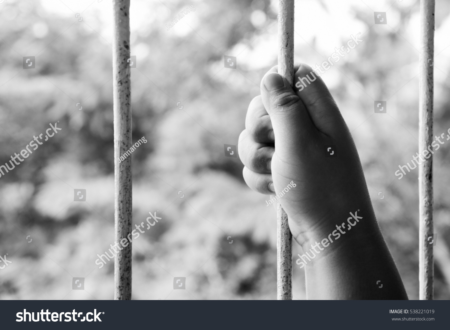 Blurred face prostitution woman grasps the bar in cage or prison with no freedom concept trying to escape or break out black and white version #538221019