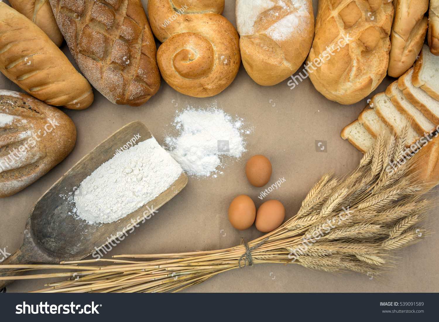 Various bread, wheat ears, scoop filled flour and eggs on brown background #539091589