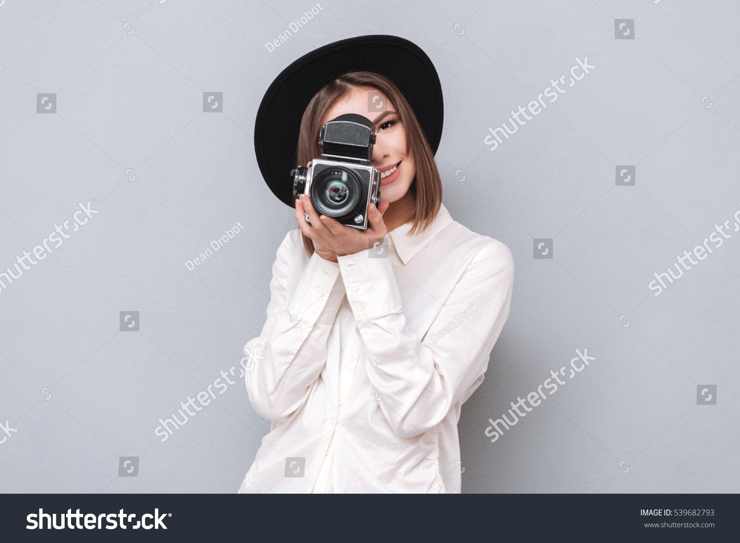 Portrait of a young smiling woman filming with retro camera isolated on the gray background #539682793