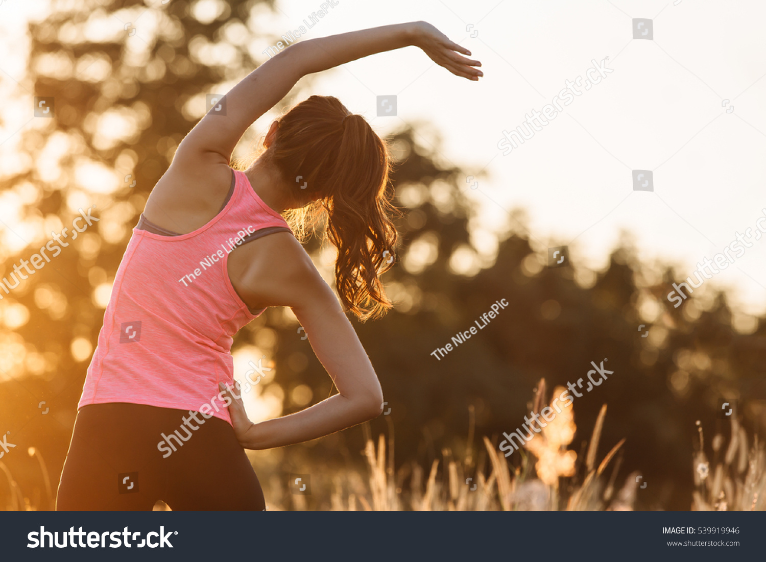 Young female workout before fitness training session at the park. Healthy young woman warming up outdoors. She is stretching her arms and looking away,hi key. #539919946