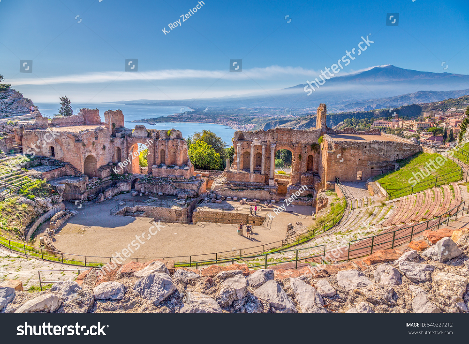 Ruins of the Ancient Greek Theater in Taormina, Sicily with the double smoke tail of the Etna extending over the the Giardini-Naxos bay of the Ionian Sea in the morning sun shine. #540227212