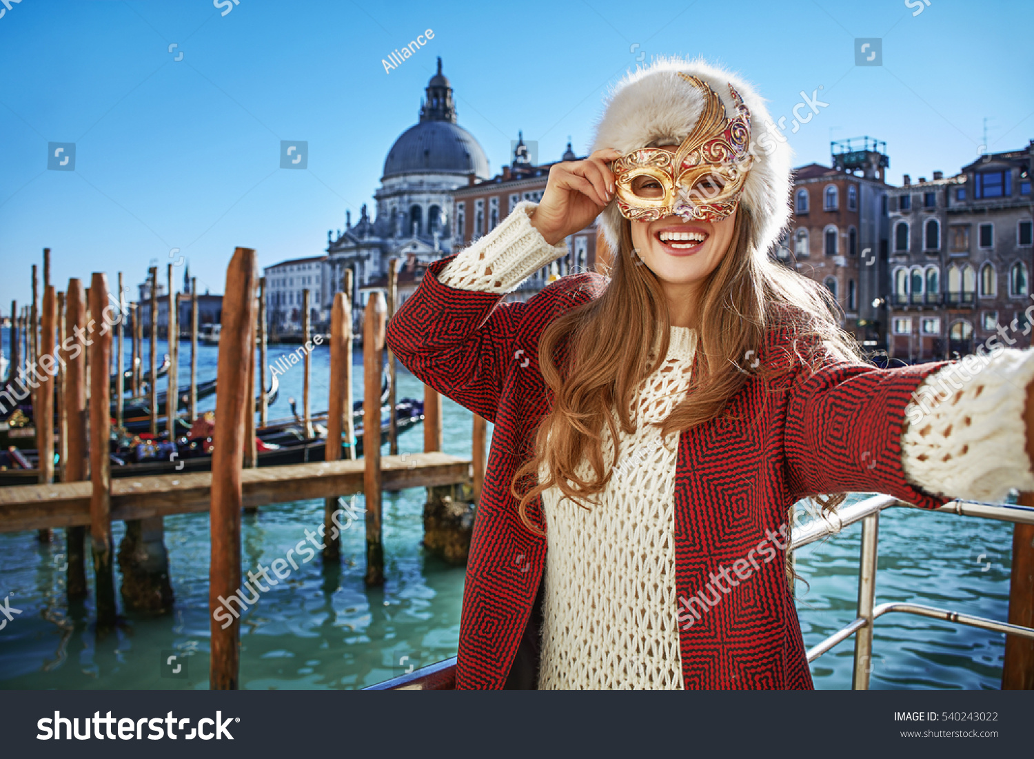 Another world vacation. Portrait of smiling elegant woman in fur hat in Venice, Italy taking selfie while in Venetian mask #540243022