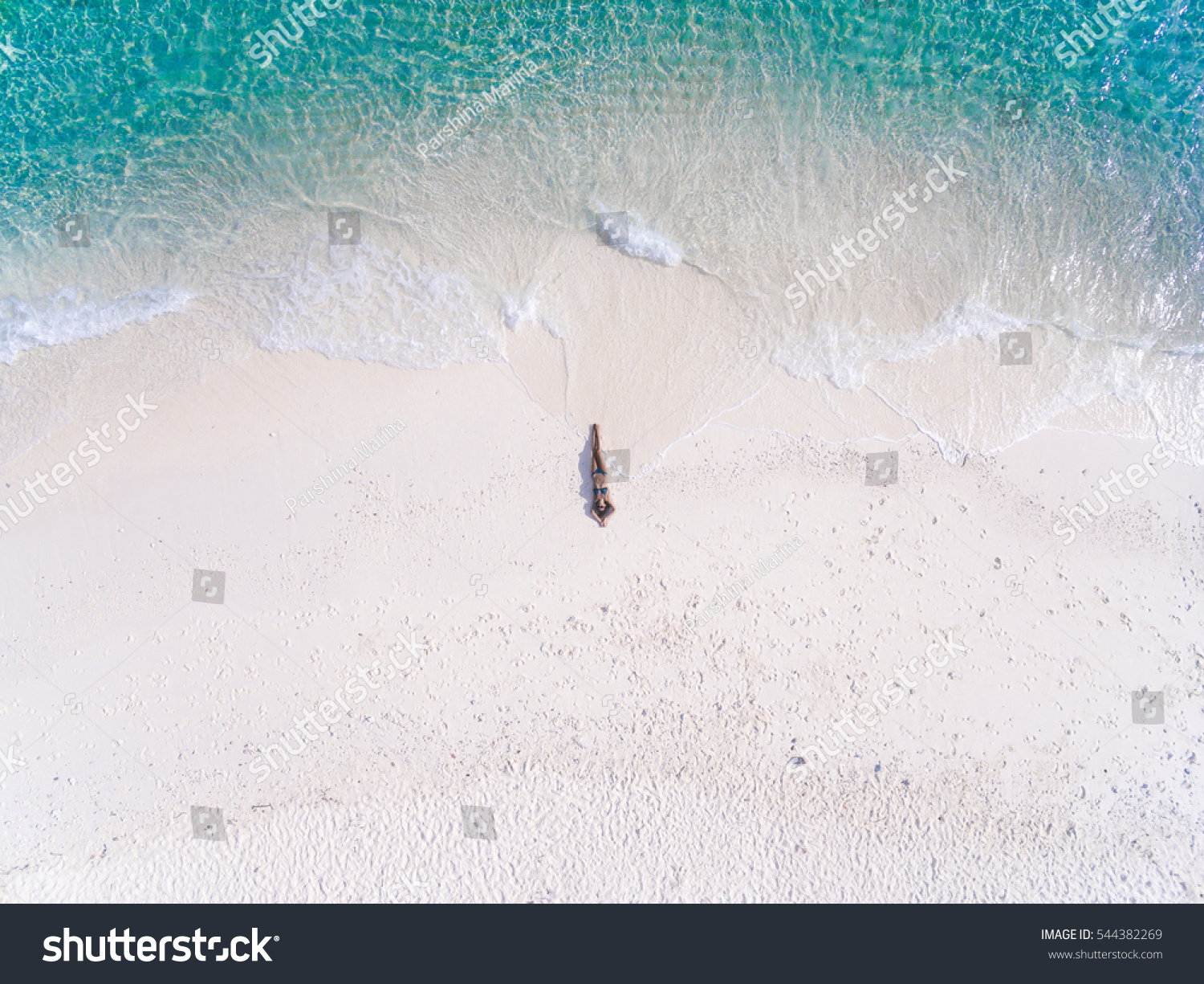 Young woman in a bikini lying on the back on the white sand near the waves of blue sea. Top view. Kai island, Andaman Sea, Phuket, Thailand. Aerial Shooting. #544382269