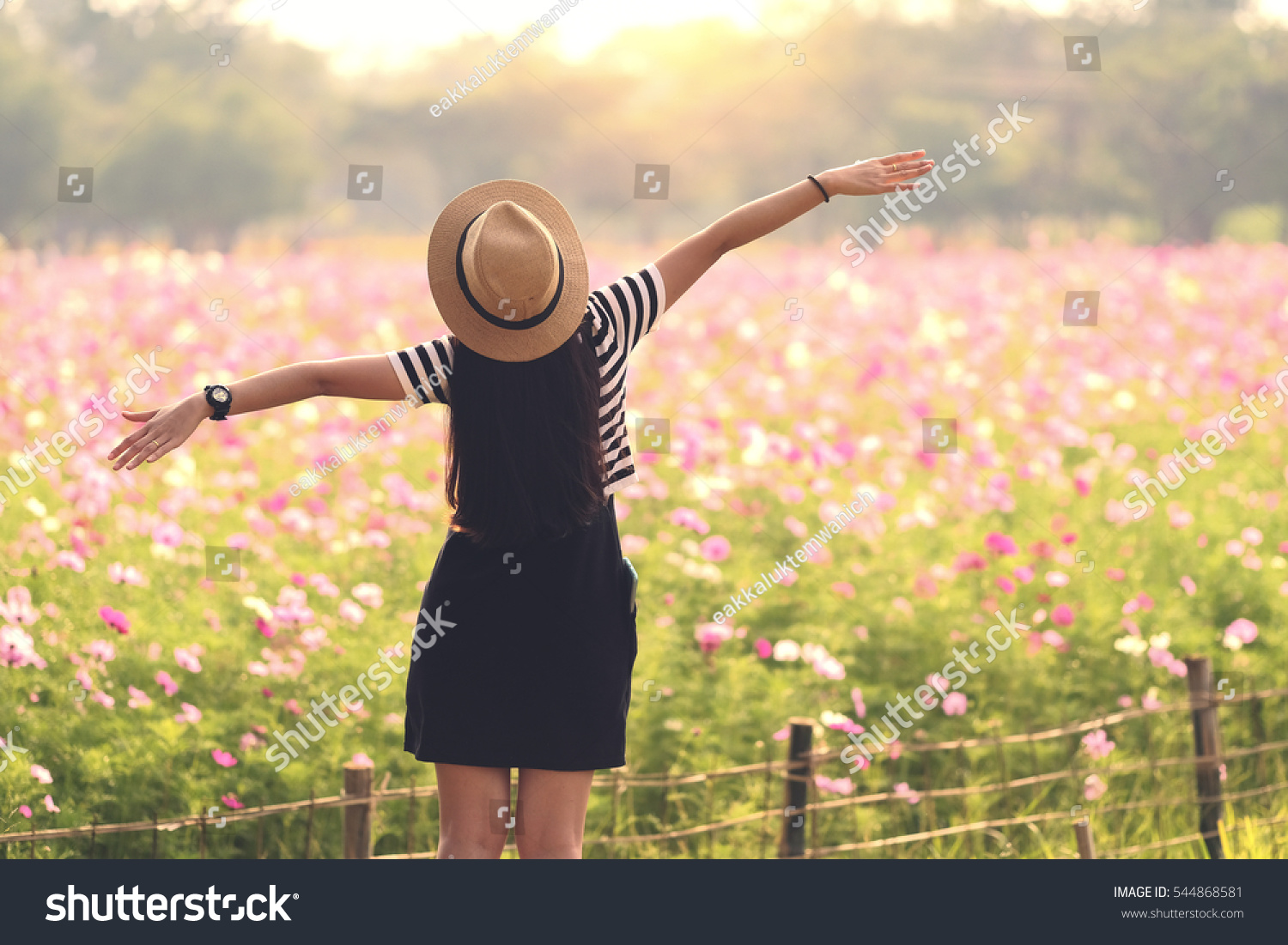 Beauty Girl Outdoors enjoying nature. Beautiful Teenage Model girl in black dress standing  on the Spring Field, Sun Light. freedom concept #544868581