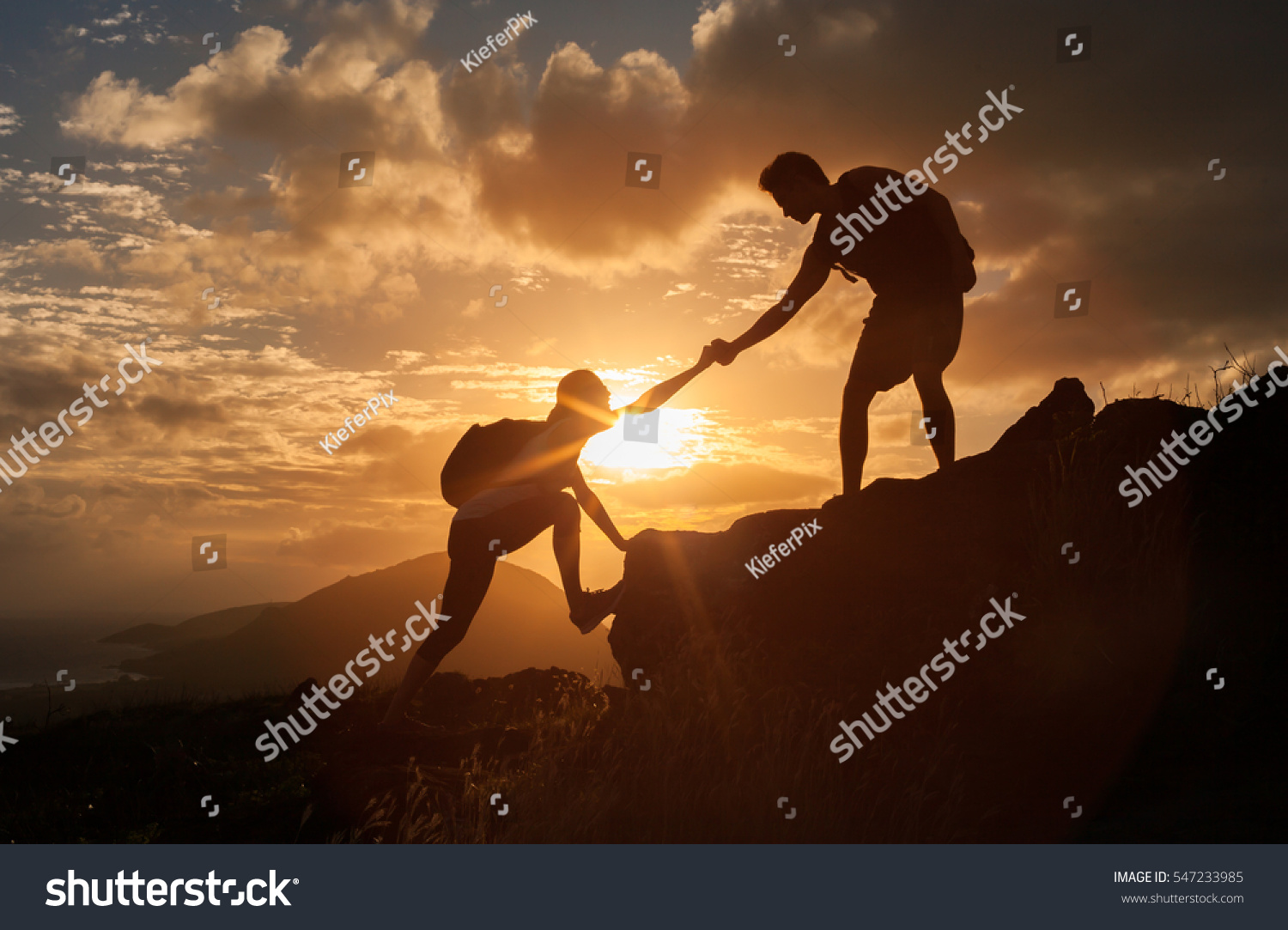 Male and female hikers climbing up mountain cliff and one of them giving helping hand.  People helping and, team work concept.

 #547233985