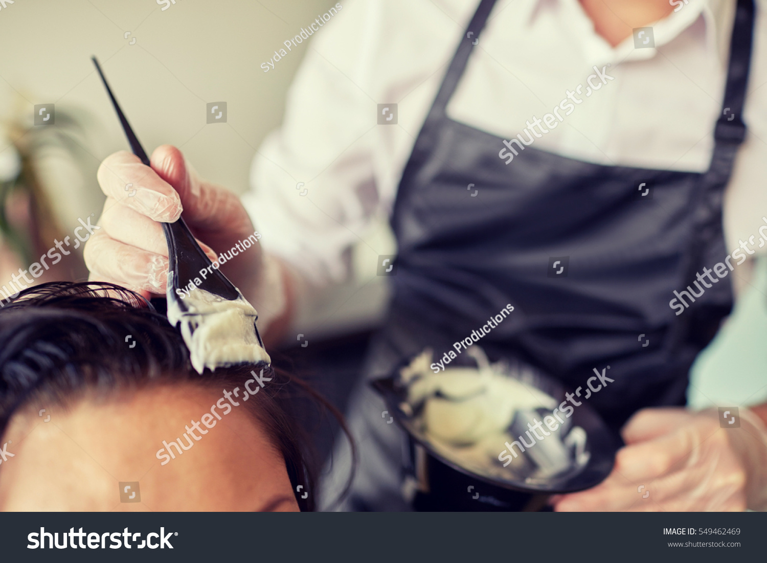 beauty and people concept - close up of stylist with hair dye and brush coloring hair at salon #549462469