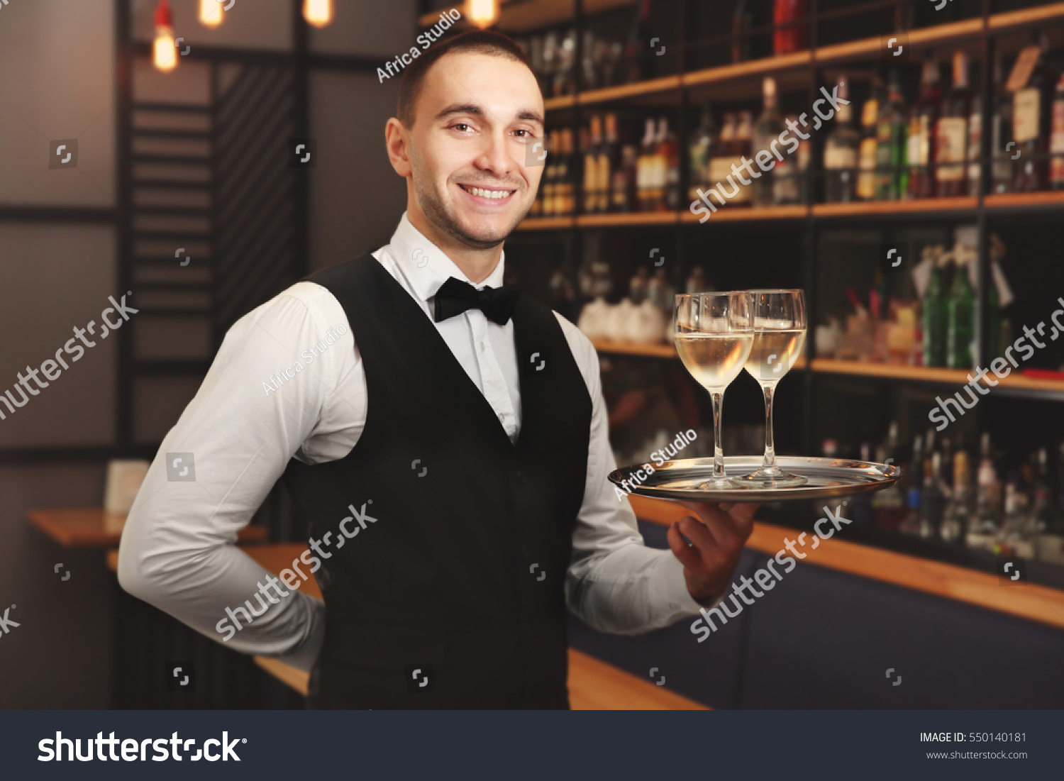 Young handsome waiter holding tray with wine glasses in the restaurant #550140181