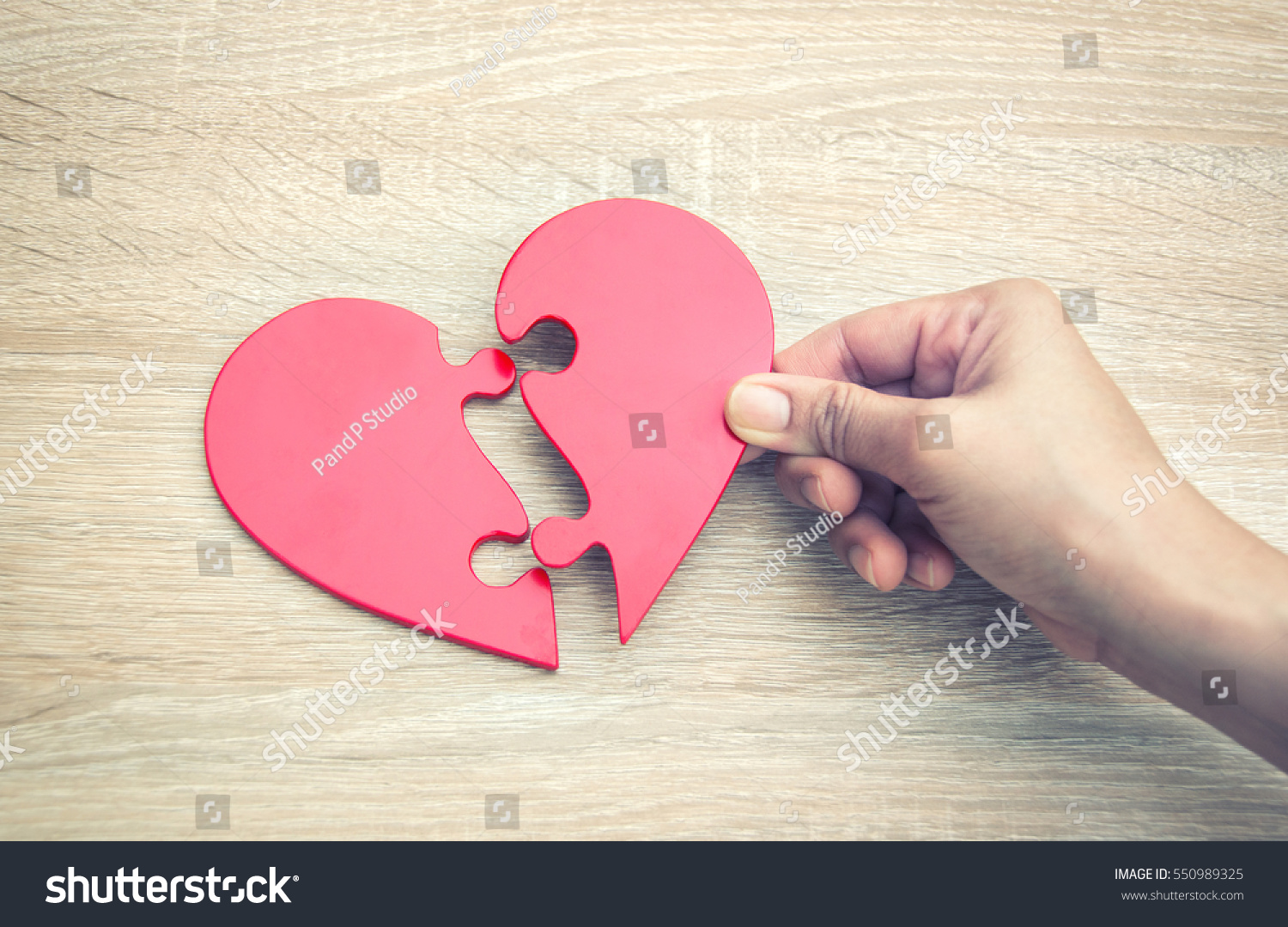 female hand matching red jigsaw heart halves on grey wooden background #550989325