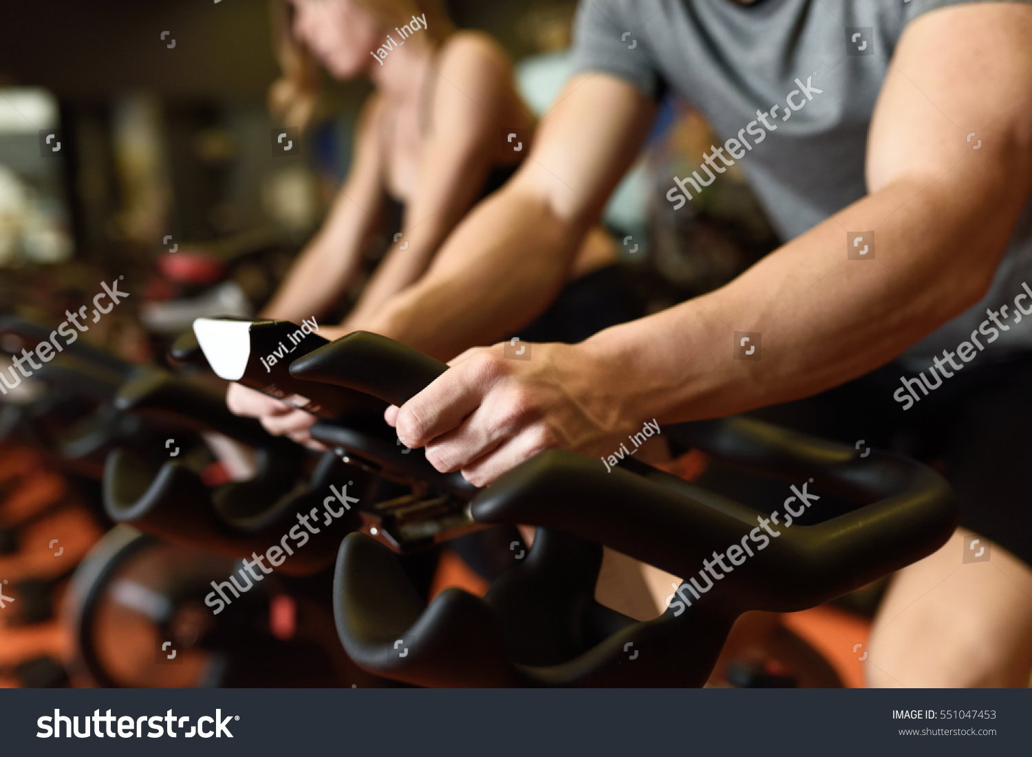 Close-up of hands of a man biking in the gym, exercising legs doing cardio workout cycling bikes. Couple in a spinning class wearing sportswear. #551047453