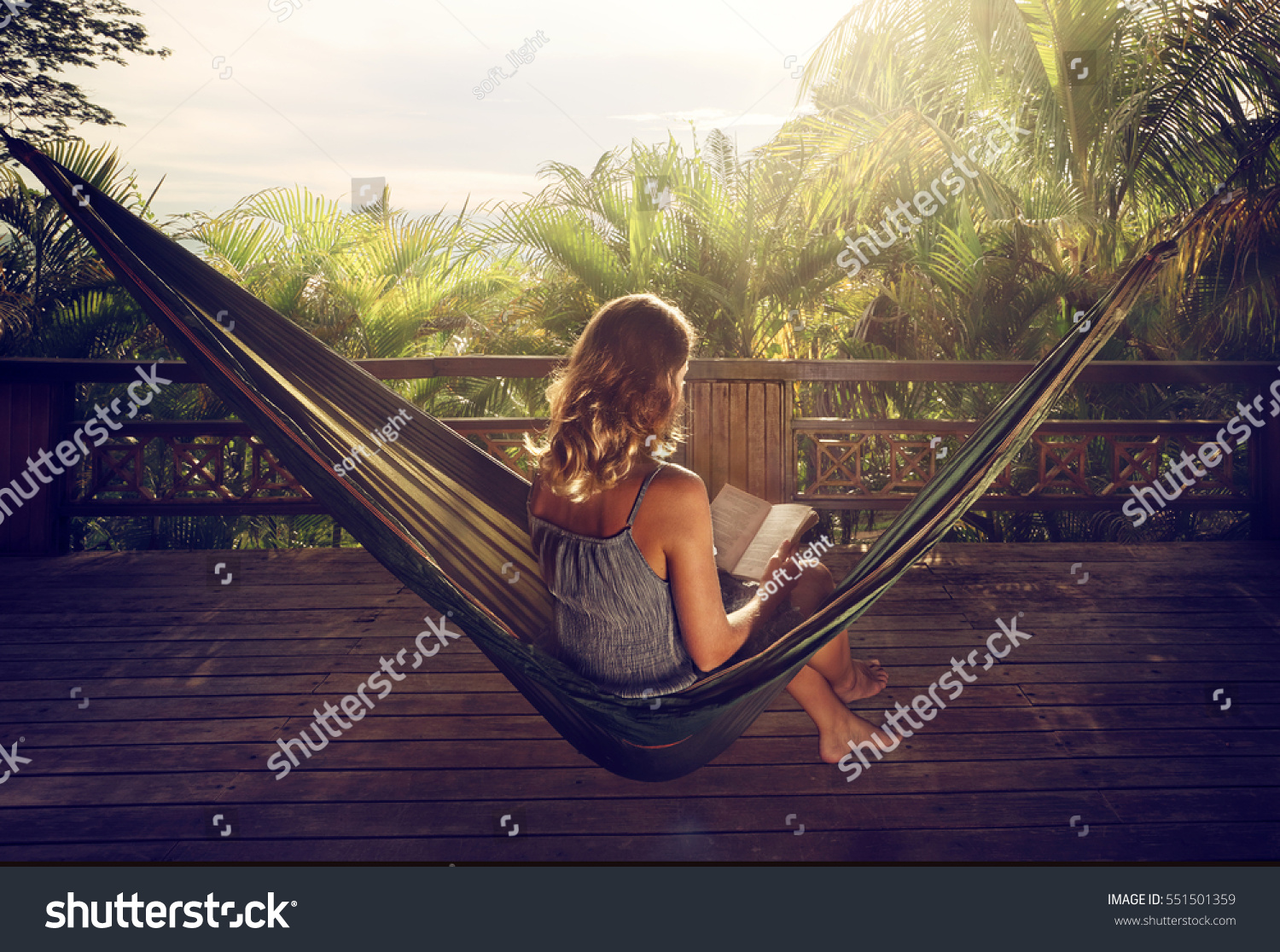 Young woman reading a book in a hammock on the terrace in the jungle at sunset #551501359
